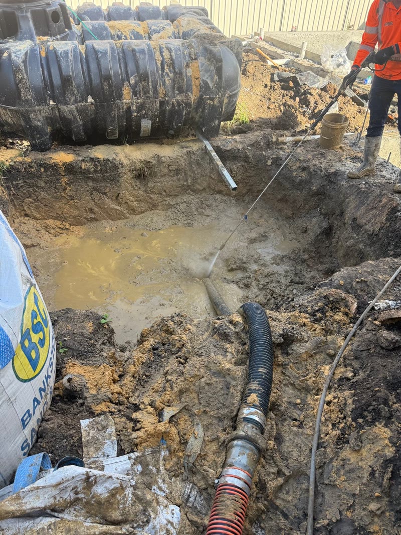 Suction hose beside an exposed pipe in wet soil