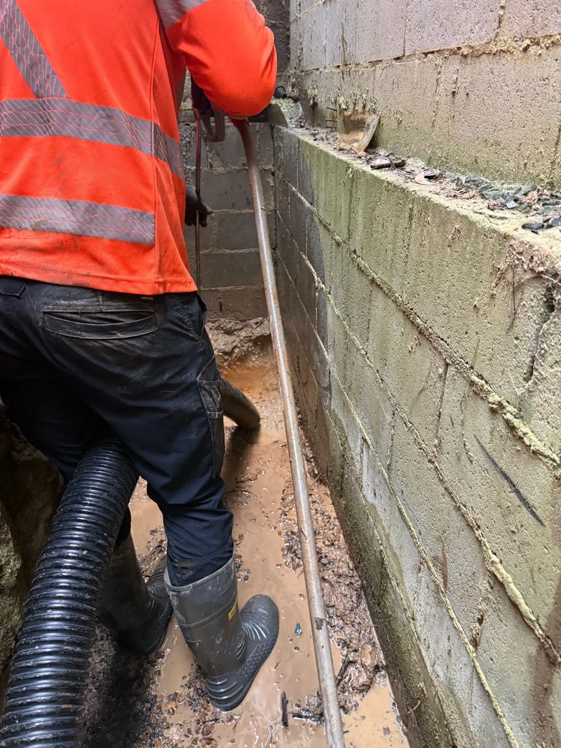 Worker guiding a vacuum hose along a narrow wall excavation
