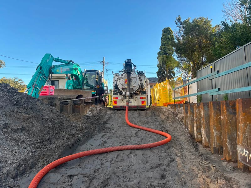Large excavator and vacuum truck working beside a shored excavation