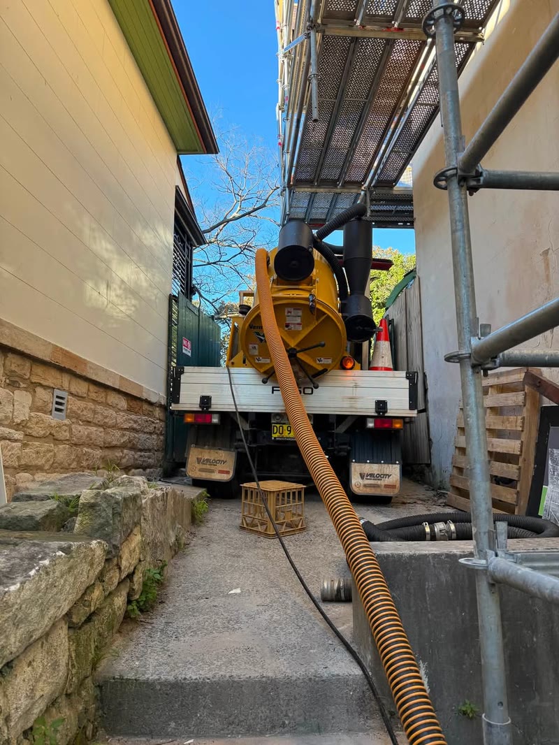Vacuum hose reaching down a narrow passage beside a building