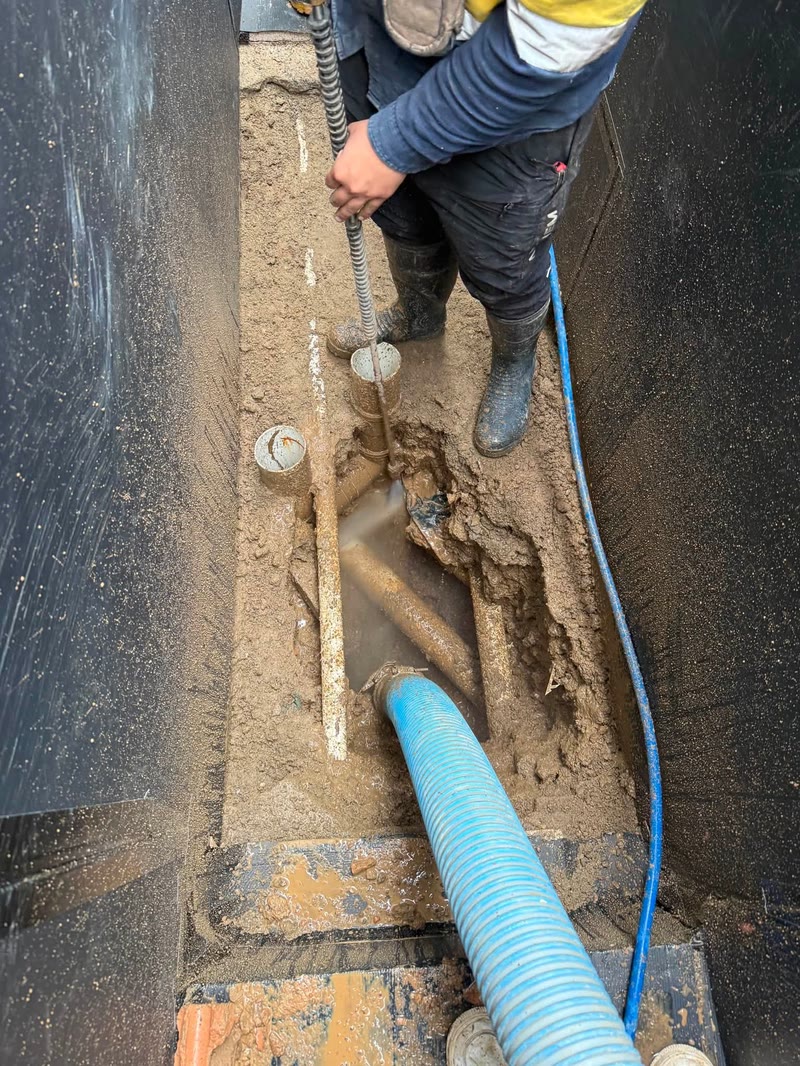 Worker using water and suction hoses in a narrow trench