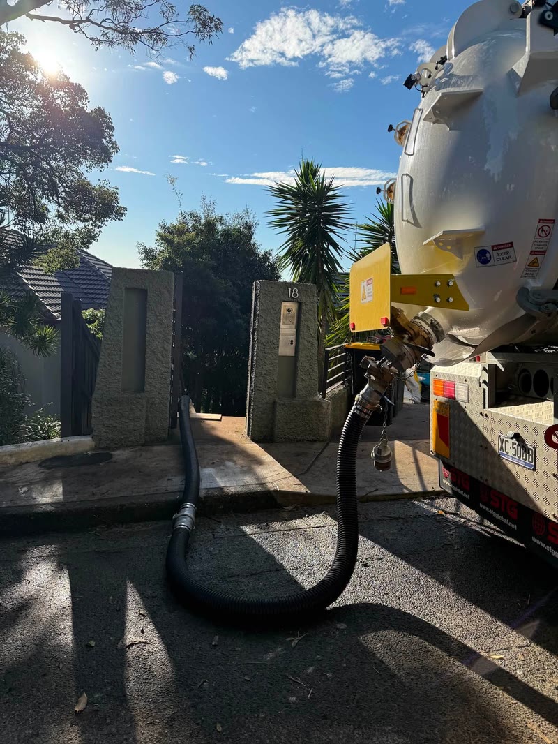 Vacuum truck outside a gate with its hose reaching the work area