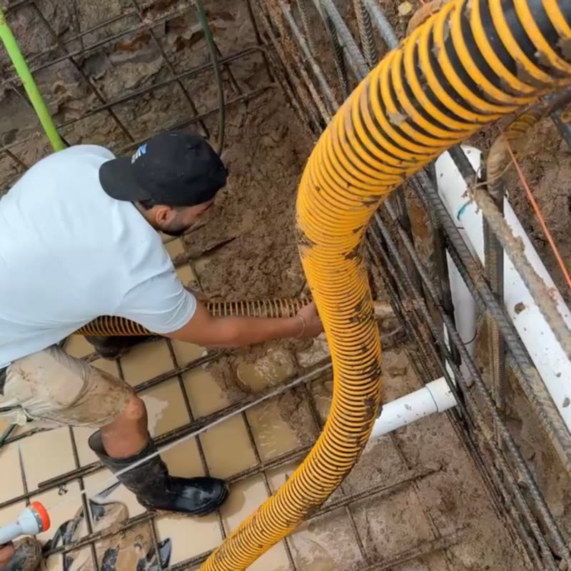 Worker guiding a suction hose between steel reinforcement bars beside exposed pipework