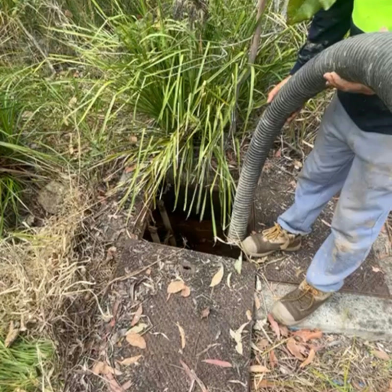 Worker guiding a vacuum hose into a small ground opening