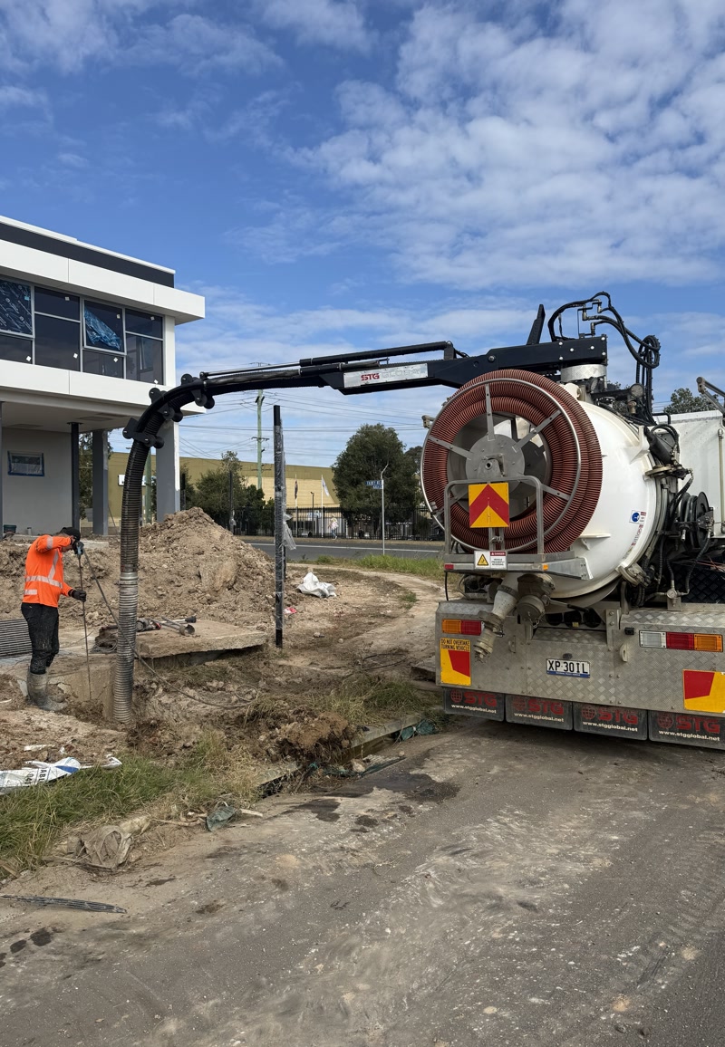 Large vacuum truck operating beside a commercial construction site