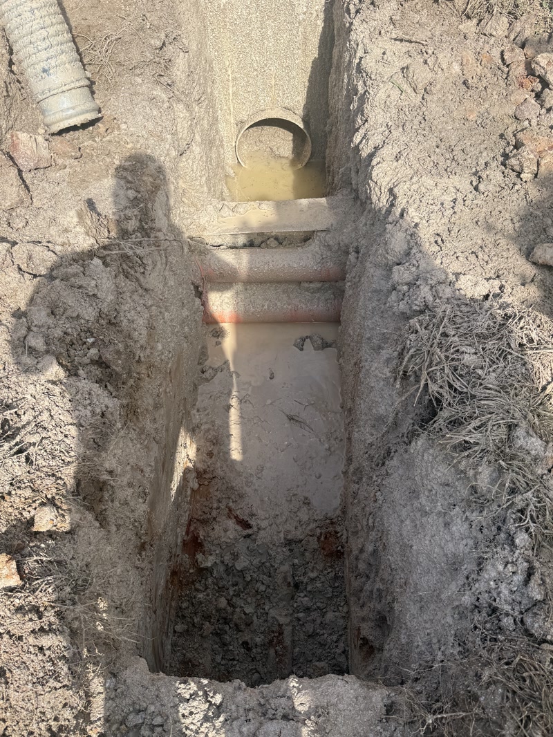 Narrow excavation exposing a marked service line and conduit beside a concrete pit