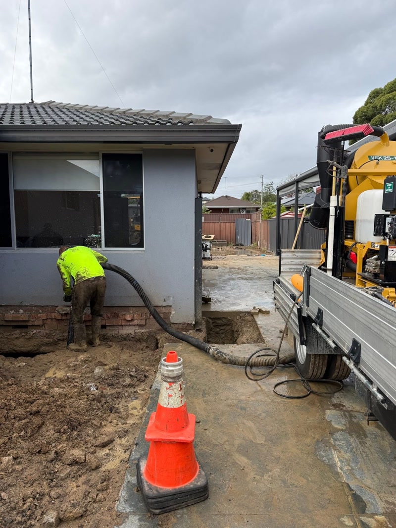 Worker excavating beside a compact vacuum unit at a home