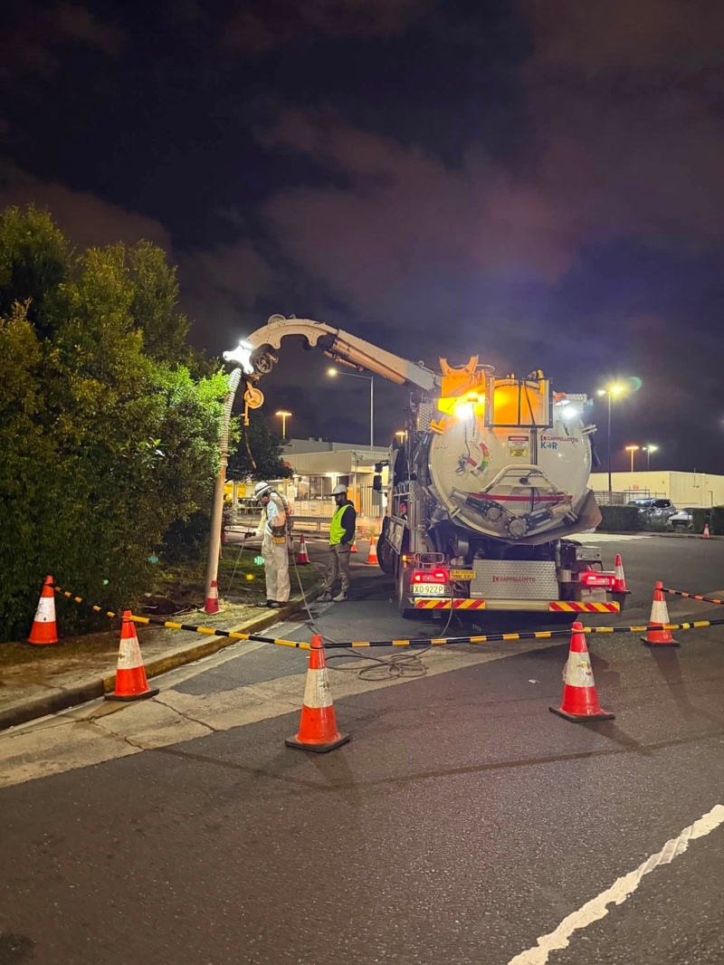 Vacuum truck working inside a coned night work zone on a suburban street