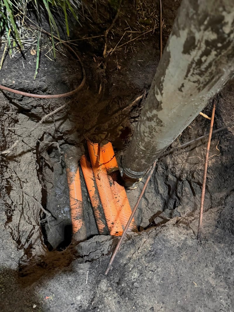 Orange electrical conduits exposed beside a vacuum hose in wet soil