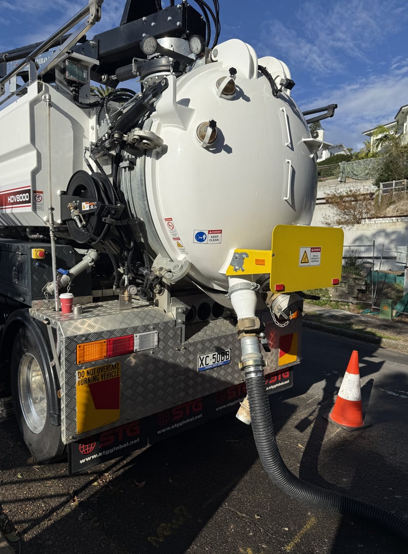 Rear of a vacuum truck with its suction hose connected on a street