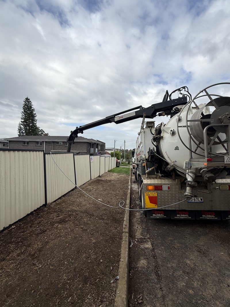 Two vacuum trucks working along a fence line with a boom extended