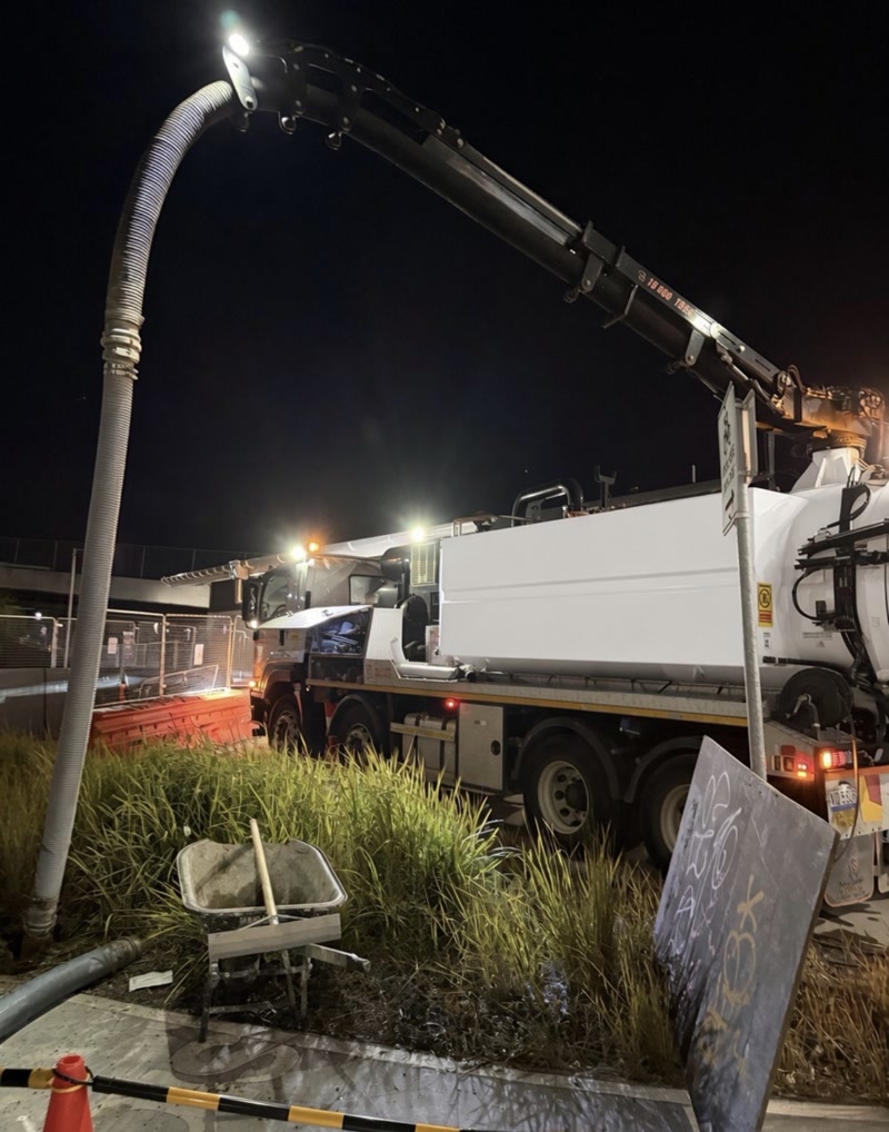 Vacuum truck and lit boom set up beside a grassed verge at night