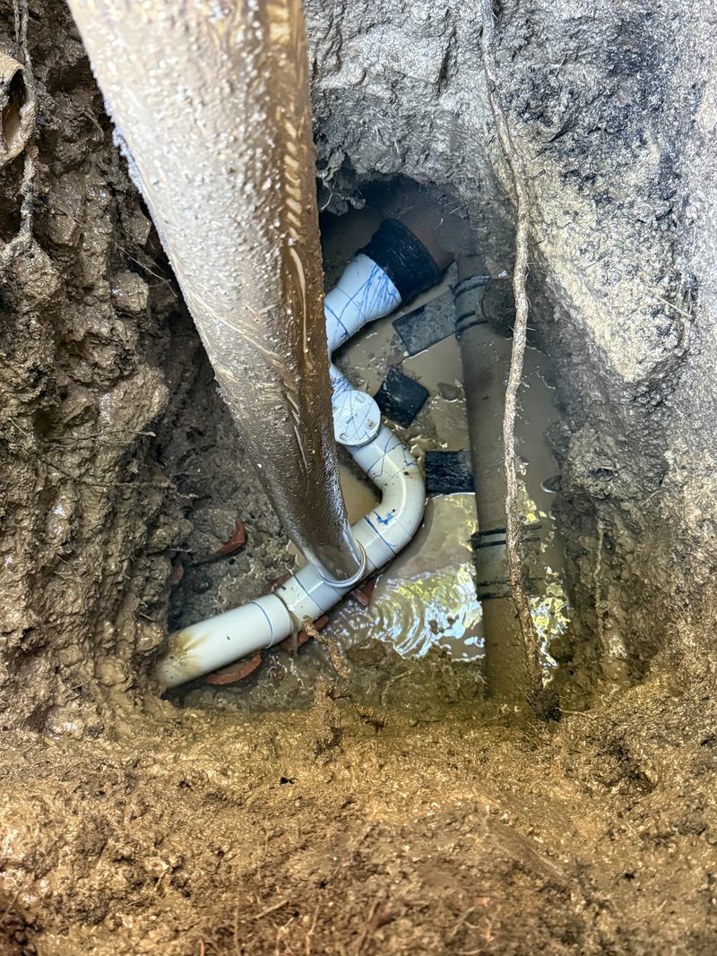 Suction hose working around exposed pipework in a water-filled rock excavation