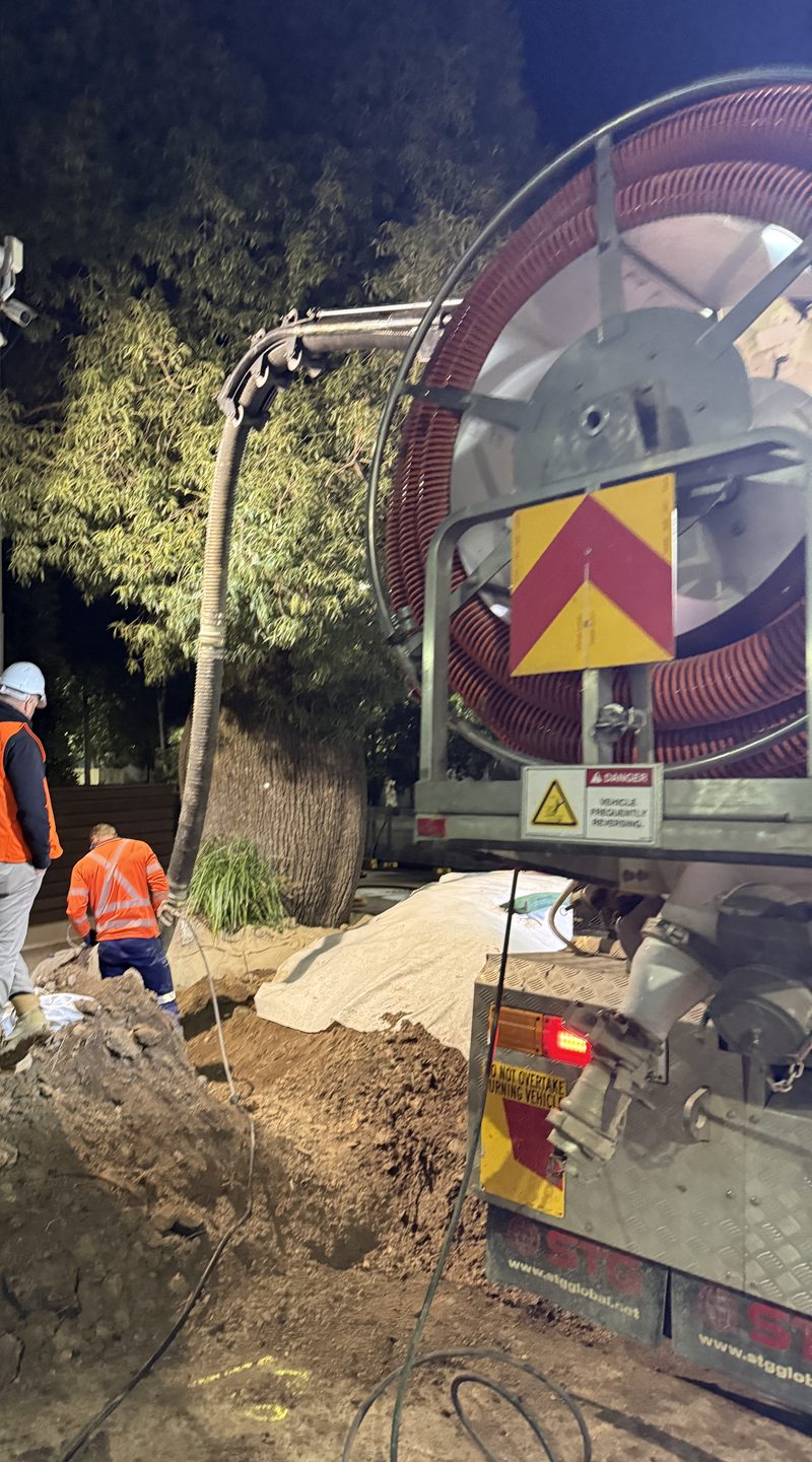 Workers beside the hose reel on a vacuum truck during night works