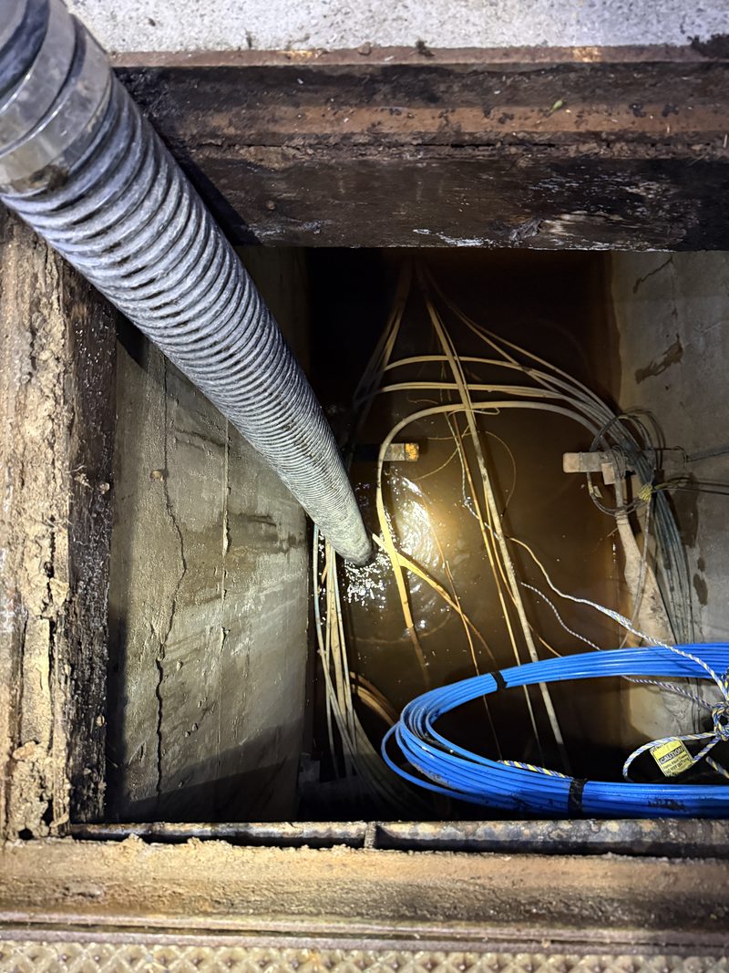 Suction hose lowered into an underground chamber holding bundled cables
