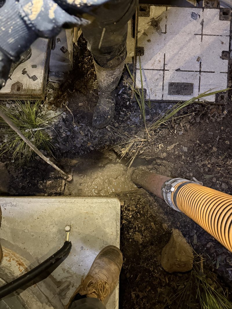 Overhead night view of a suction hose clearing wet spoil beside lifted concrete pit lids