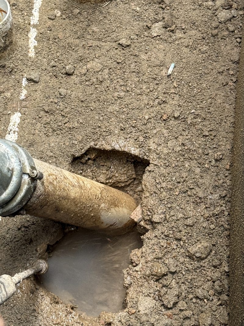 Suction hose and water lance opening a small excavation in clay beside a marked service line