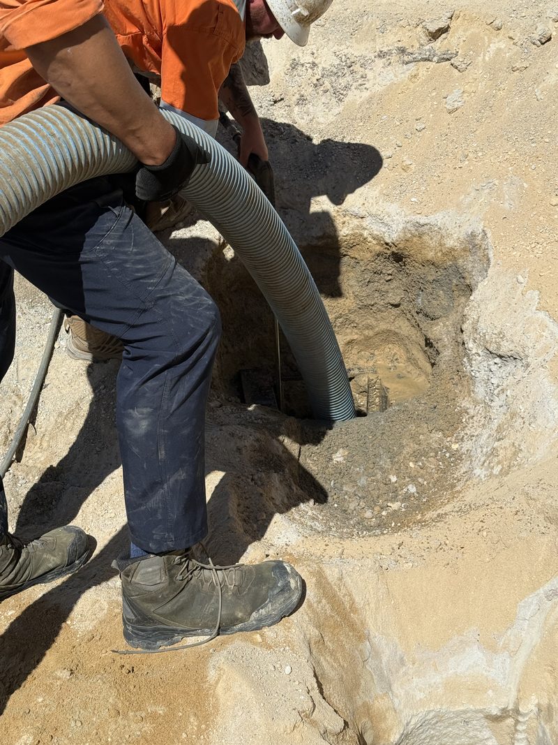 Worker guiding a suction hose into an excavation cut through sandstone