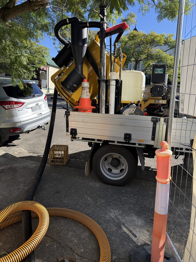 Compact vacuum unit on a truck tray working beside temporary fencing on an inner-city street